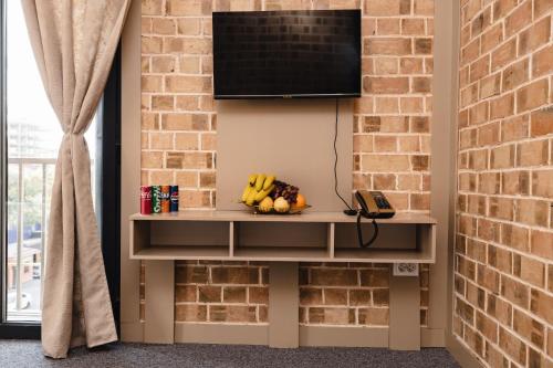 a television on a brick wall with a table with fruit at Art Air Hotel in Tashkent