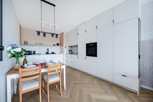 Manufaktura Suites - 76m2, Parking, AirCon - by Rentujemy في لودز: مطبخ بخزائن بيضاء وطاولة وكراسي خشبية