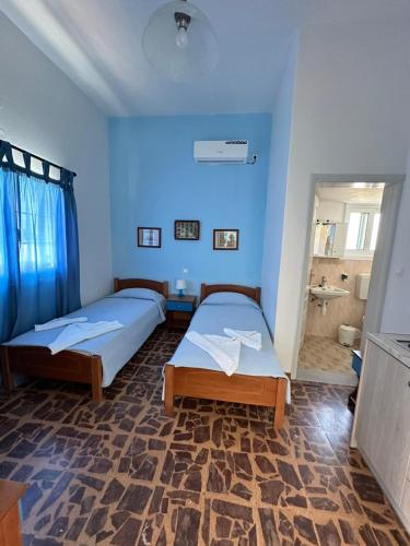 two beds in a room with blue walls and a bathroom at Rena's Garden Rooms in Lipsoi