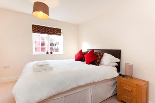 a bedroom with a large white bed with red pillows at DBS Serviced Apartments - The Coach House in Castle Donington