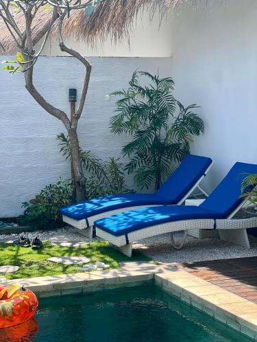 a pool with two blue lounge chairs next to a swimming pool at Villa Kayu in Gili Air