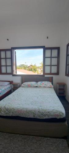 Un dormitorio con una cama con una ventana grande. en Arandu, en Peruíbe