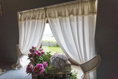 a window with white curtains and a chair and flowers at Palascìa Wellness Relais in Otranto