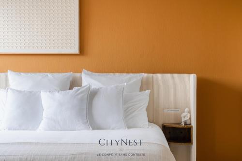 a bed with white pillows and an orange wall at Studio Premium CityNest in Strasbourg