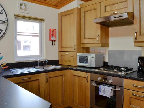 a kitchen with wooden cabinets and a sink and a microwave at Lodge G- Uk33093 in Dinnet
