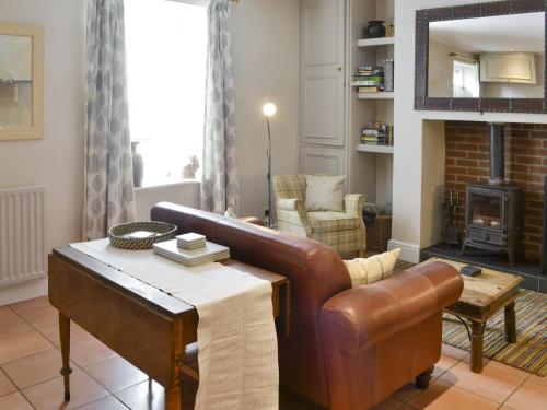 sala de estar con sofá de cuero y chimenea en Youngers Cottage, en Warkworth