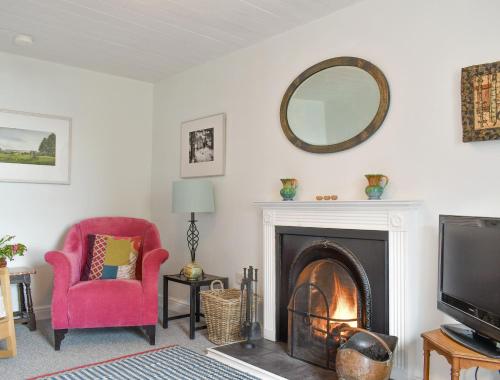 un salon avec une cheminée, une chaise rose et un miroir dans l'établissement Seaton Cottage, à Collieston
