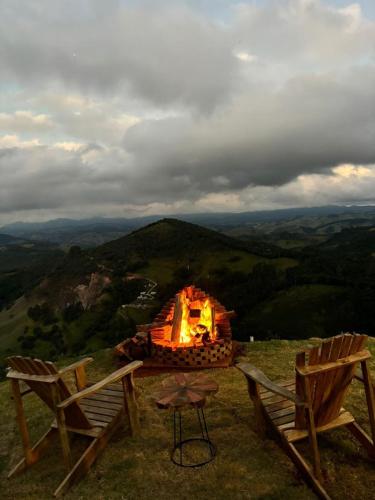 two chairs and a fire pit on top of a mountain at Chalé Manacá in Sapucaí-Mirim