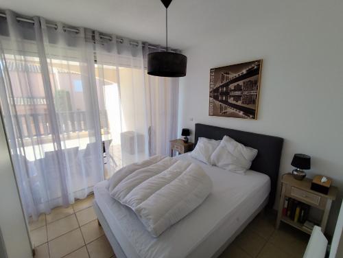 une chambre avec un lit blanc avec une grande fenêtre dans l'établissement Résidence Les Reflets, à Saint Cyprien Plage
