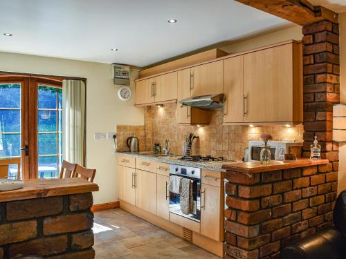 a kitchen with wooden cabinets and a brick wall at Poppy Cottage - Uk40102 in Dunvant