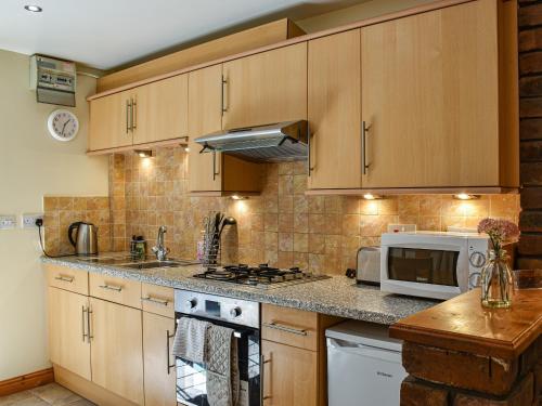 a kitchen with wooden cabinets and a microwave at Poppy Cottage - Uk40102 in Dunvant