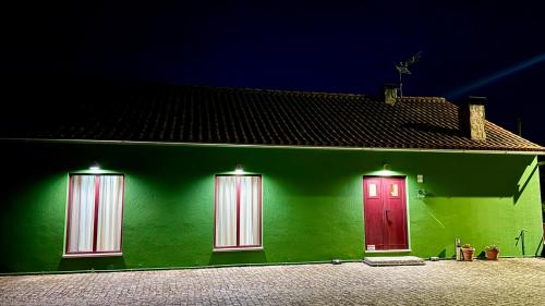 a green house with two red doors on it at Raízes da Vinha - Quartos & Chalé na Serra da Estrela in Carragozela