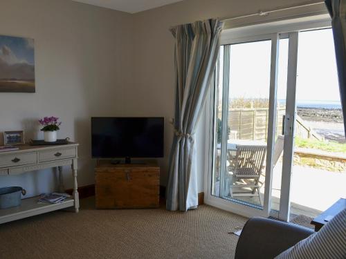 a living room with a television and a sliding glass door at Limpet Cottage in Boulmer