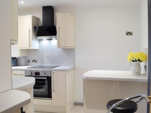 a kitchen with white cabinets and a vase of flowers at Princess Court Apartment in Llanelli