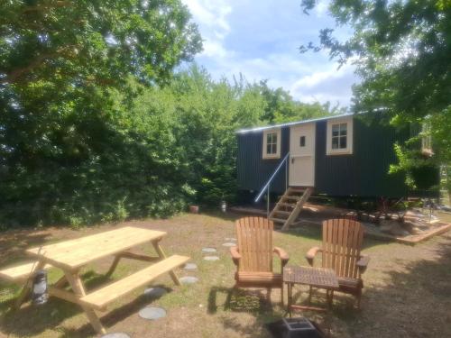 a picnic table and two chairs in front of a tiny house at Hill Top Hideaway Shepherds Hut with Hot Tub in Woodham Mortimer