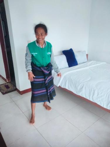 a woman standing in a room next to a bed at Lucky guest house in Kelimutu