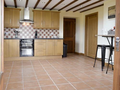a kitchen with wooden cabinets and a tile floor at Llofft Storws in Valley