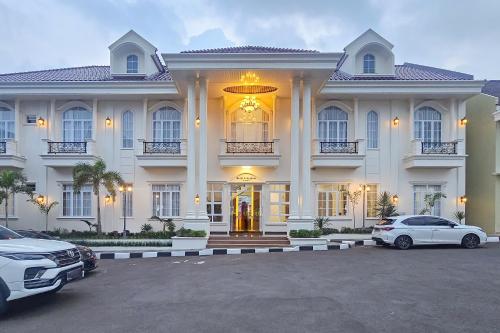 a large white building with two cars parked in a parking lot at Sans Vibes Hotel Sulanjana Syariah Sukabumi in Krawang