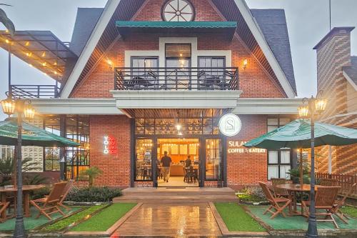 a building with tables and umbrellas in front of it at Sans Vibes Hotel Sulanjana Syariah Sukabumi in Krawang