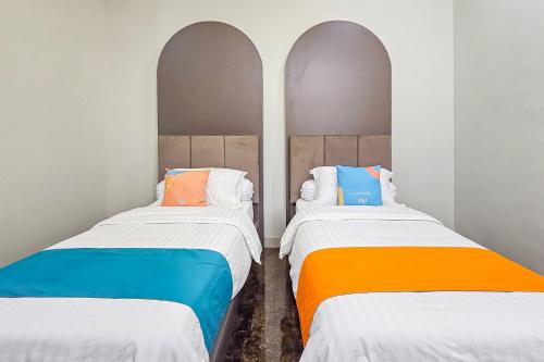two beds with colorful pillows in a room at Sans Vibes Hotel Sulanjana Syariah Sukabumi in Krawang