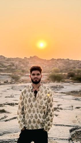 a man standing on a beach with the sunset in the background at Lily Homestay in New Hampi