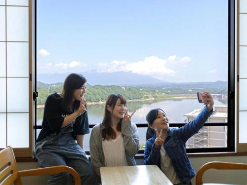 three women sitting at a table taking pictures of a window at Hotel Shion in Morioka