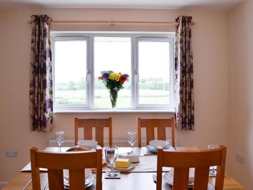 a table with chairs and a window with a vase of flowers at Dolview in Penybont