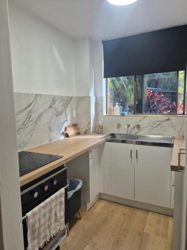 a kitchen with white cabinets and a sink and a window at Dunes Apartment Unit 8- GROUND FLOOR WITH POOL VIEW in Coffs Harbour