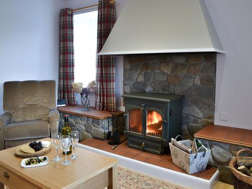 a living room with a fireplace and a table with wine glasses at Glebe Cottage in Urray