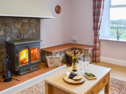 a living room with a fireplace and a table with wine glasses at Glebe Cottage in Urray