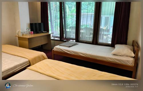 a room with two beds and a desk with windows at Homestay Triniti in Lembang