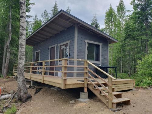 a tiny house with a large deck in the woods at Mini cottage by lake Saimaa in Enonkoski