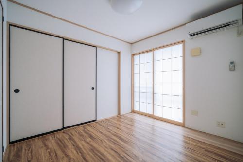 an empty room with glass doors and wooden floors at Comfort Miyabi -4号棟 in Yomitan