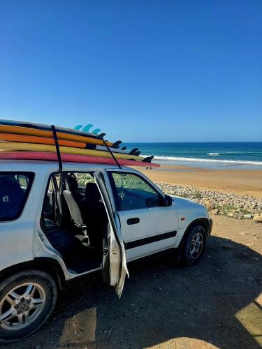 a white car with a surfboard on top on a beach at Moroccan Boho Surf House in Agadir