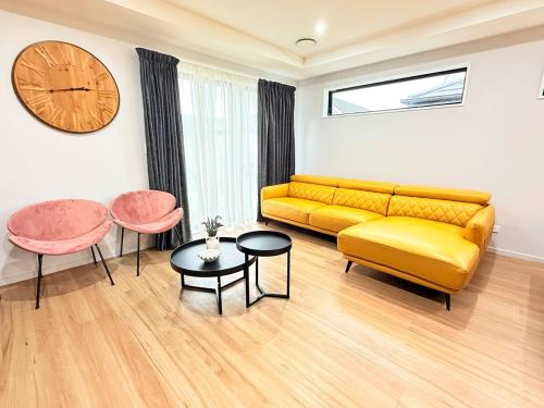 a living room with a yellow couch and two tables and a clock at Tranquil 4 Bed Family Retreat 5Min To Airport in Christchurch