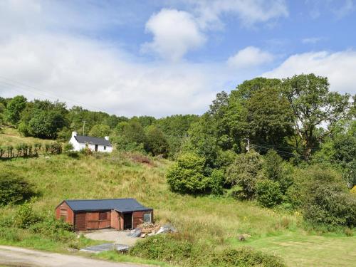 a small shed on a hill with a house in the background at The Old Croft House in Strontian