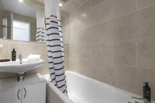 La salle de bains est pourvue d'une baignoire blanche, d'un lavabo et d'une baignoire. dans l'établissement Le Triolet - Centre-ville - Balcon avec vue, à Chamonix-Mont-Blanc