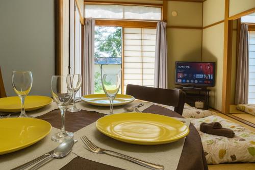 a dining room table with yellow plates and wine glasses at Oiwake House 1B in Karuizawa