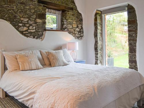 a bedroom with a white bed with a stone wall at Pigaway Cottage in Petrockstow