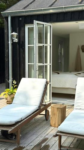 a porch with two chairs and a bed on a deck at Wooden House With Animals And Kayaks Near Aalborg in Aalborg