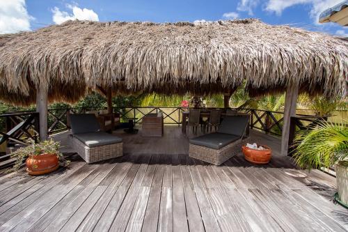 una terraza de madera con 2 sillas y techo de paja en Casa El Tropico, en Kralendijk
