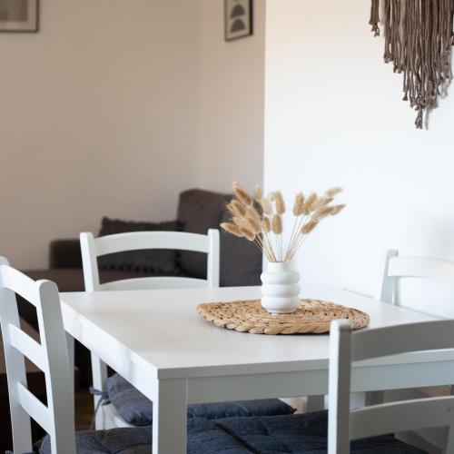 a white dining room table with white chairs and a vase with flowers at Houlia home διαμερίσματα με δωρεάν χώρο στάθμευσης in Andros