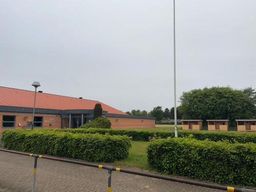 a brick building with a red roof and some bushes at Hærvejshallen Hytte 3 in Bække