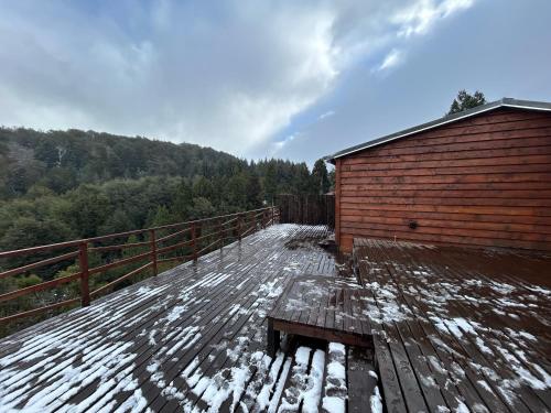 a wooden deck covered in snow next to a building at Cabaña de montaña Amber in San Carlos de Bariloche
