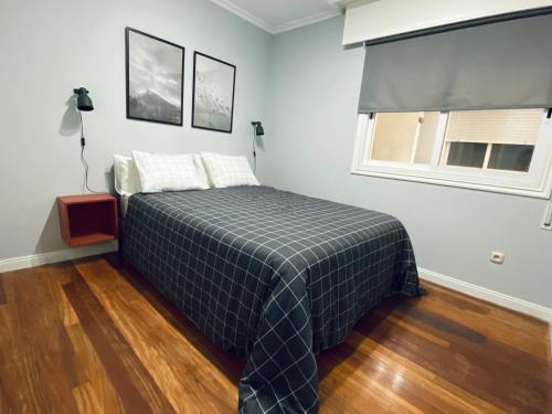 a bedroom with a bed with a checked blanket and a window at Piso Céntrico 120m2 + parking propio (O Grove) in O Grove