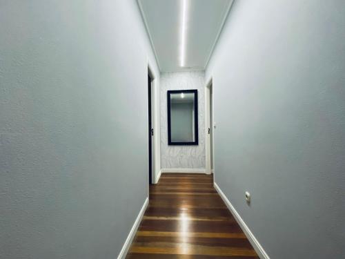 a hallway with white walls and wooden floors and a mirror at Piso Céntrico 120m2 + parking propio (O Grove) in O Grove