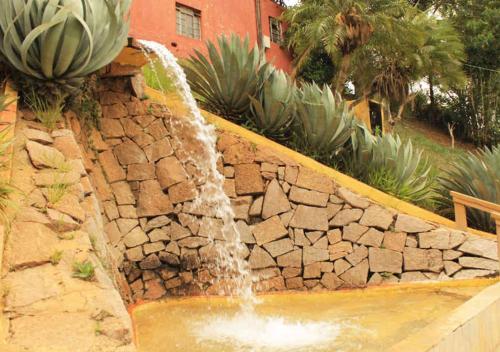 a water fountain in a garden with a stone wall at Chalé Gratidão - Camping Carrion - ITU in Itu