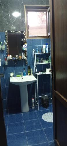 La salle de bains est pourvue de carrelage bleu, d'un lavabo et d'une fenêtre. dans l'établissement Nino's Guesthouse, à Batoumi