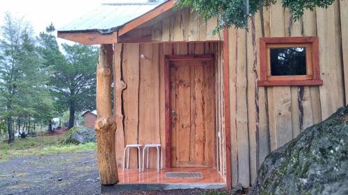 a small wooden building with a door and two stools at Refugio entre Coihues in Melipeuco