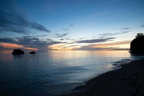 a sunset on the beach with rocks in the water at 陽月-Hizuki- in Nakijin